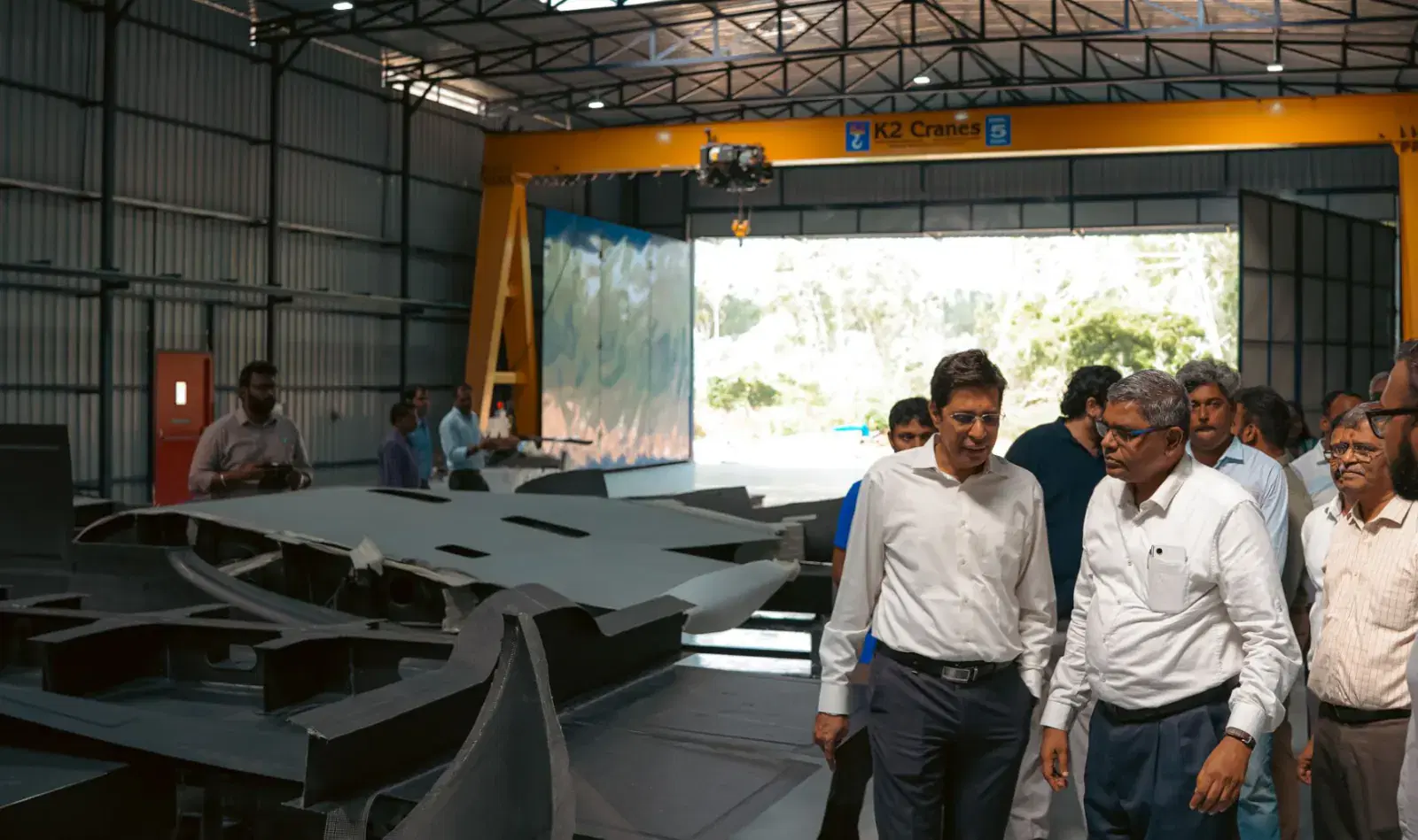 The founding team walking through the hangar past laid-out composite airframe panels